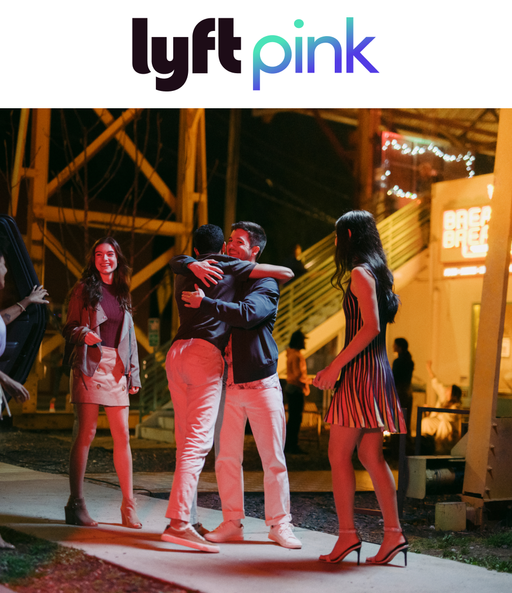 Four young adults greet each other with hugs and smiles at night, near a lit building. A Lyft Pink logo is above the image. 